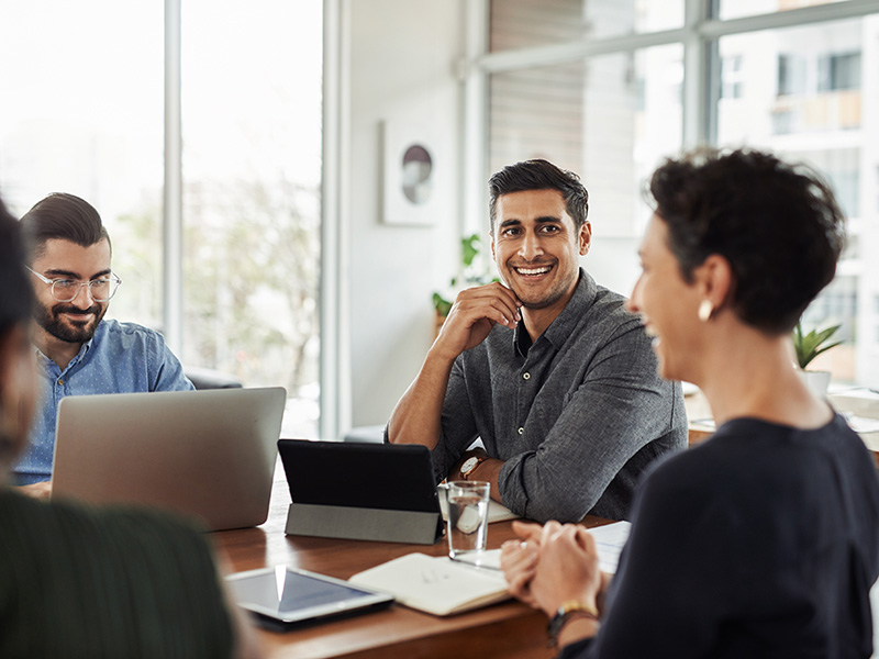 Office professionals sitting at a meeting table with their laptops